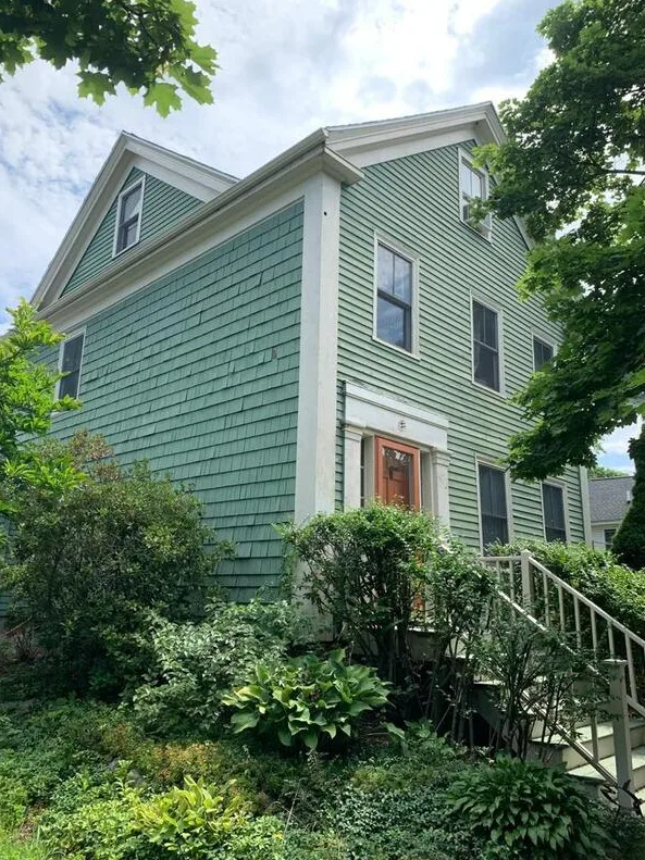 Cedar shingle colonial painted sage green with cream trim and a coral front door.